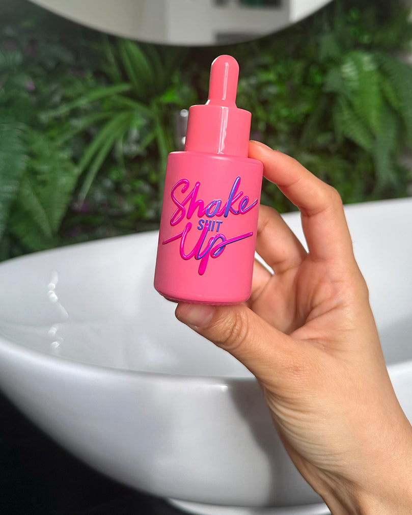 Person holding Shake It Up Facial Oil in a bathroom – vibrant red dropper bottle shown in hand, energising blend for confidence and tired, dull skin.