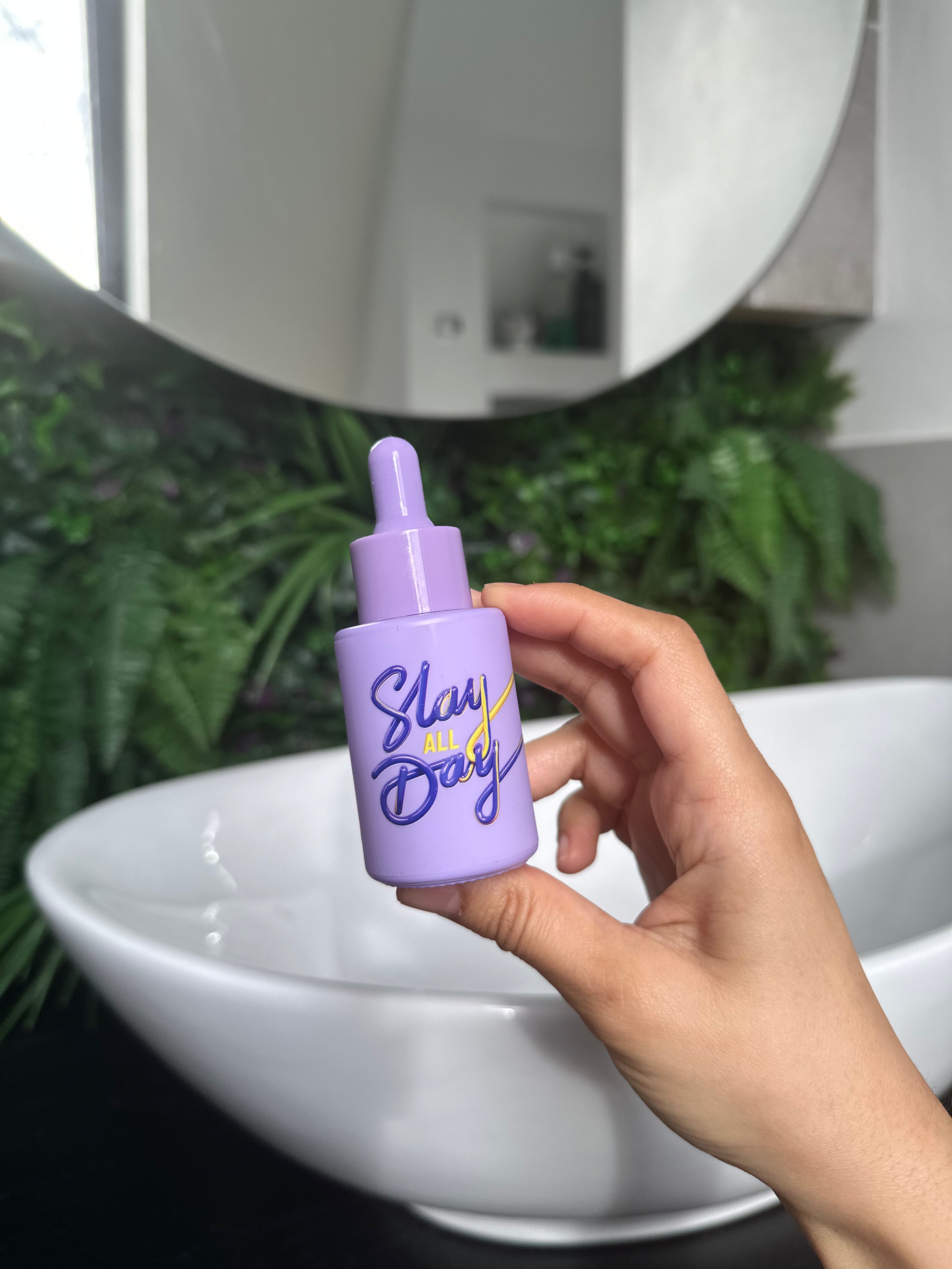 Person holding Slay All Day Facial Oil in a soft bathroom light – purple bottle in hand, formulated to strengthen skin and emotional resilience.