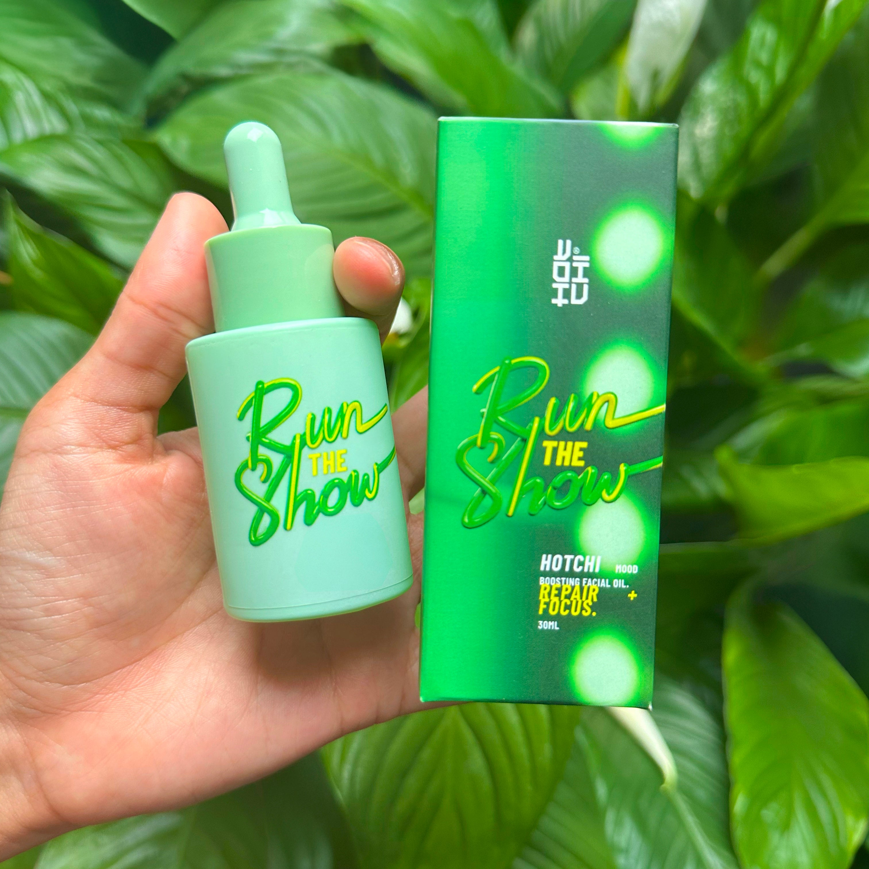 Hand holding HotChi’s green Run The Show facial oil bottle, designed to boost mental focus and clarity through a soothing skincare ritual.