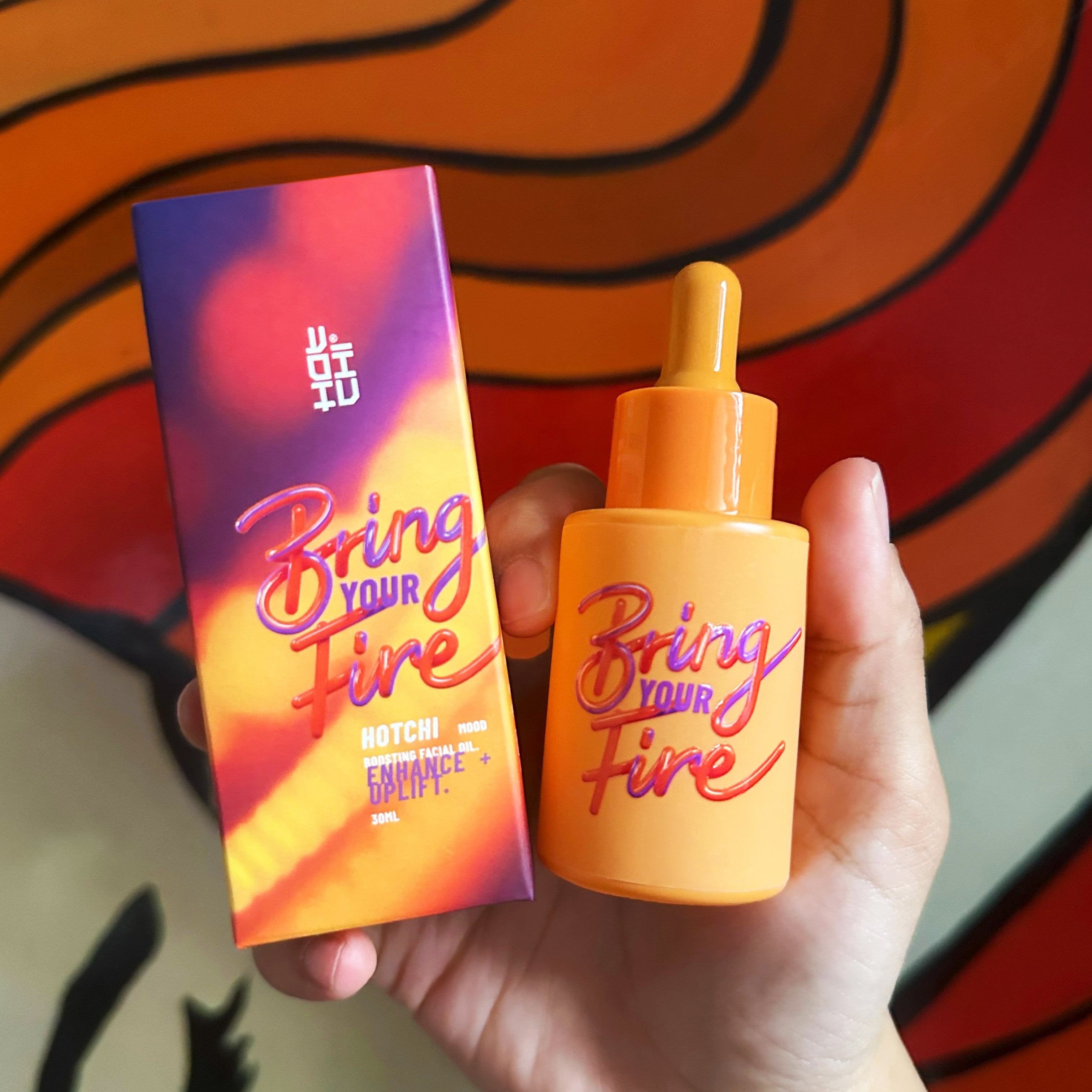 Hand holding HotChi’s Bring Your Fire facial oil in its vibrant orange bottle, designed to calm anxiety and soothe both skin and senses.