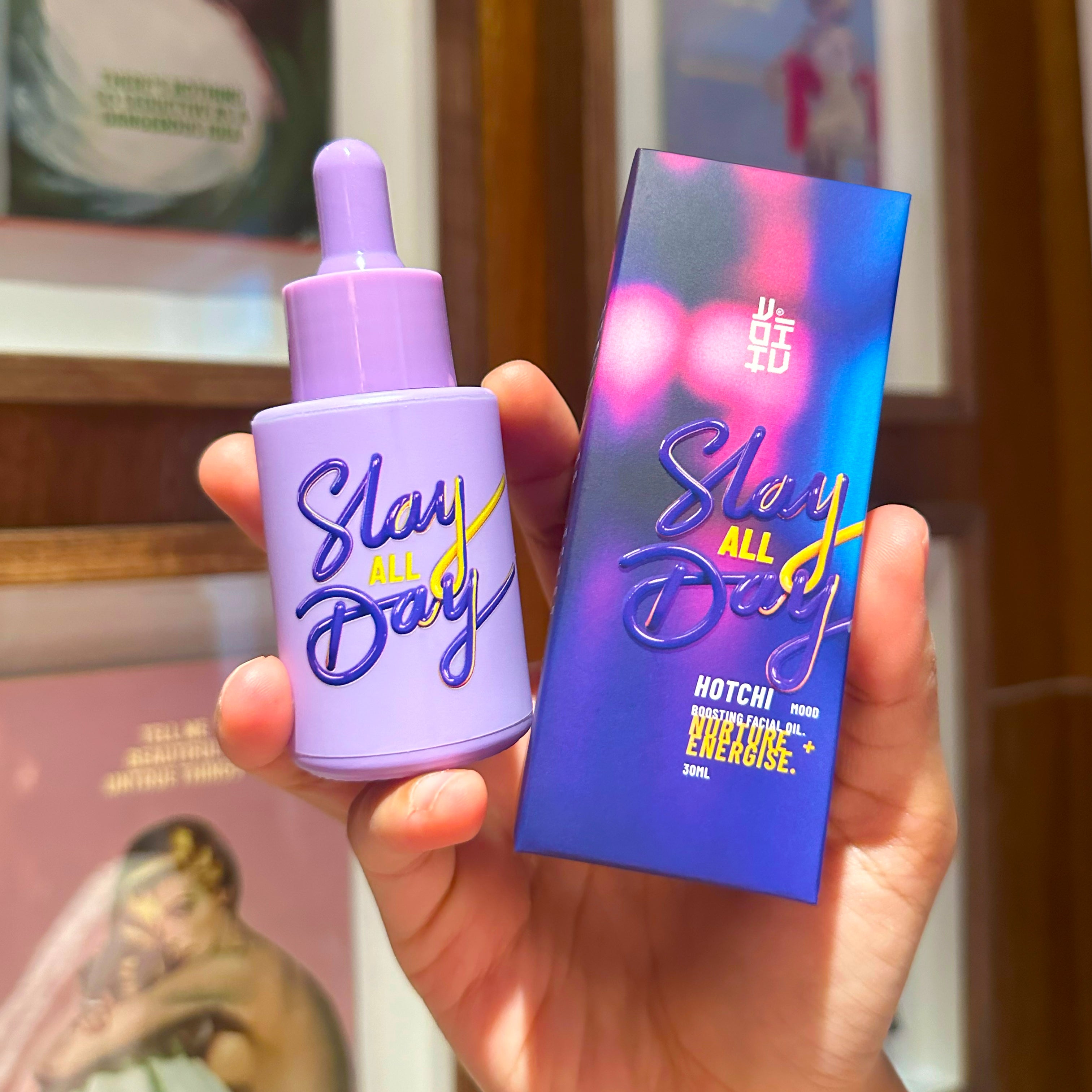 Hand holding HotChi’s Slay All Day facial oil in a rich purple bottle, formulated to boost emotional strength and empower your daily routine.