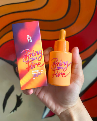 A hand holding the Bring Your Fire Facial Oil bottle, symbolizing self-care and calmness with HotChi's mood-boosting skincare.