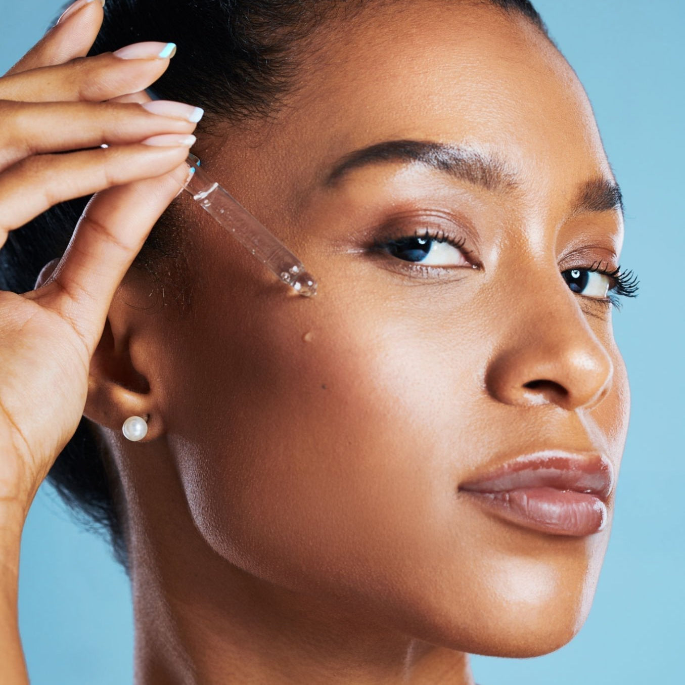 Close-up of a woman gently applying facial oil to her face, highlighting a glowing skincare routine and natural skin hydration.