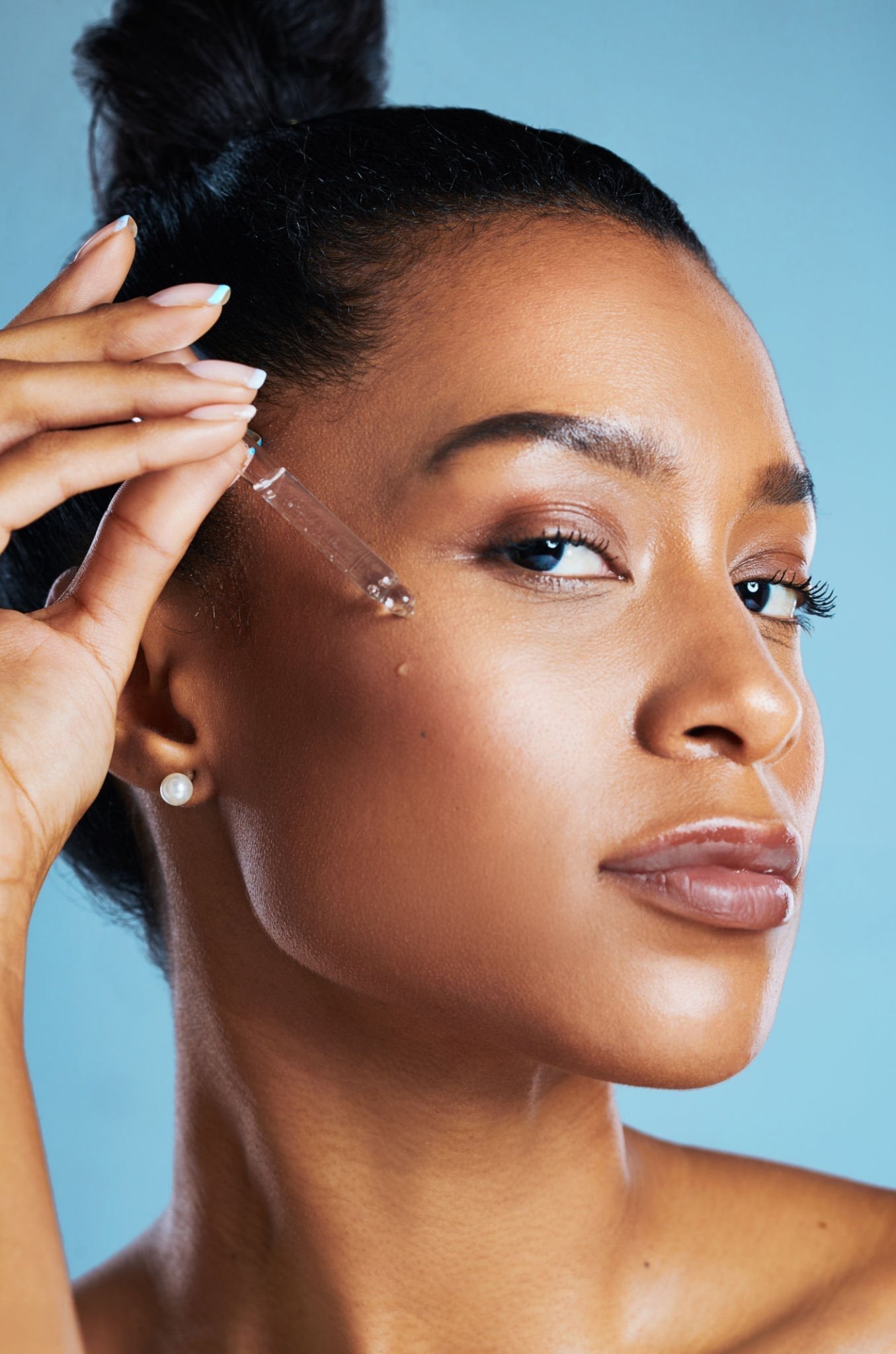 Close-up of a woman gently applying facial oil to her face, highlighting a glowing skincare routine and natural skin hydration.