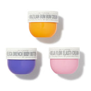 Three cosmetic jars from Veu de Janeiro arranged on a white background: a yellow-orange Brazilian Bum Bum Cream jar at the top, a purple Gelicia Drench Body Butter jar at lower left, and a pink Beja Flor Elasti-Cream jar at lower right.