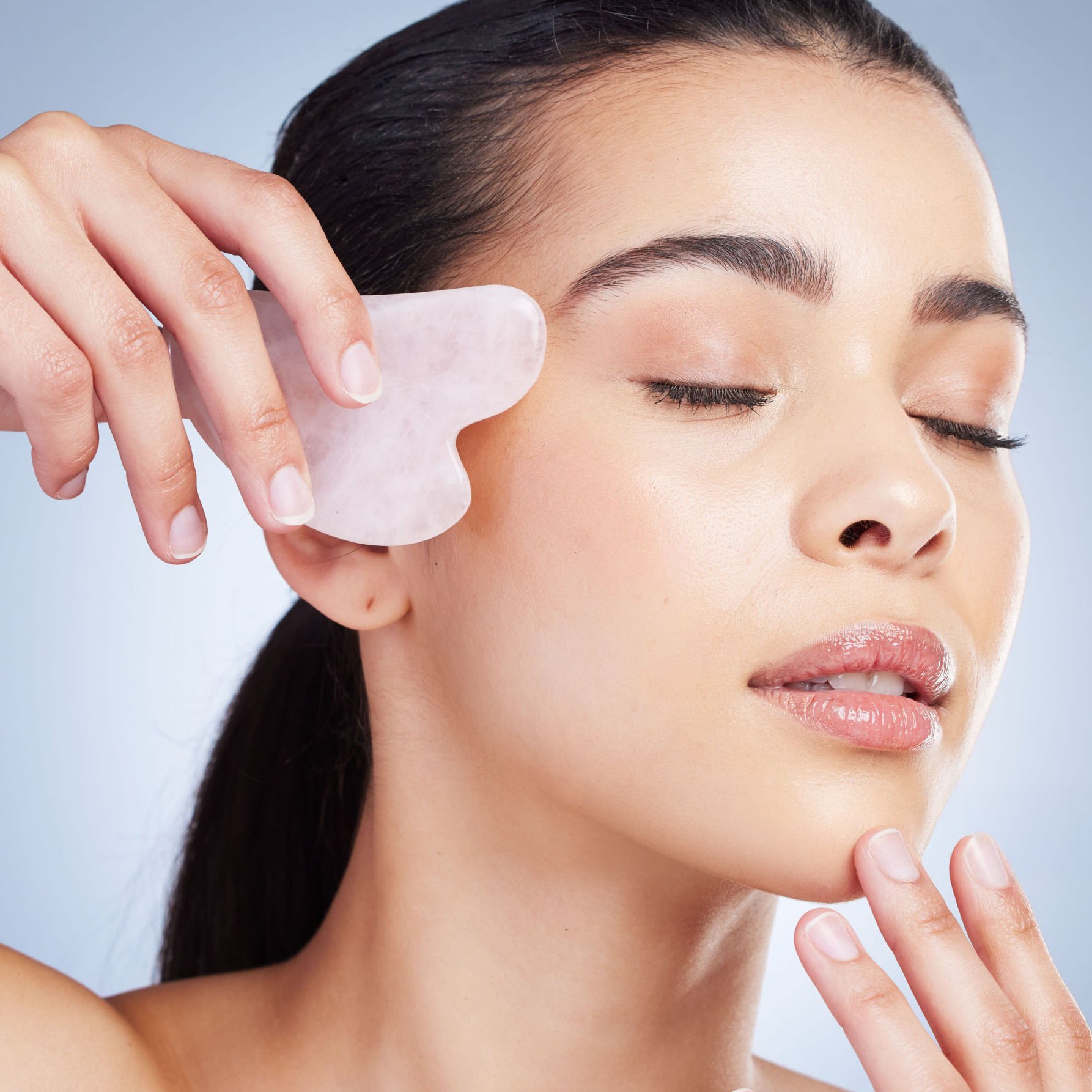 White woman massaging her forehead with a stainless steel gua sha, promoting relaxation and improved circulation.